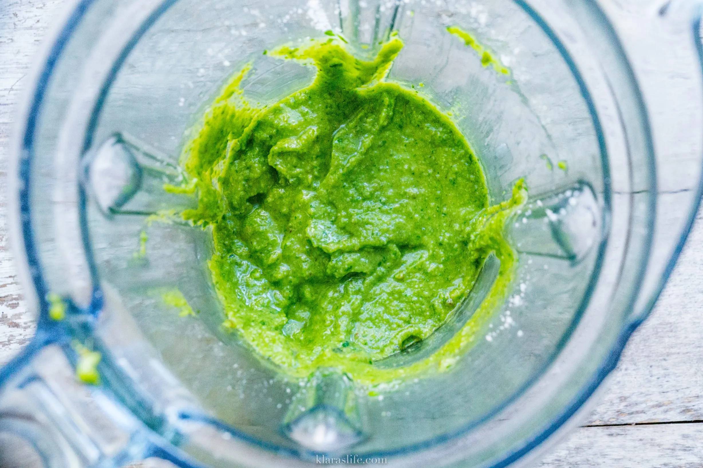 Nahaufnahme eines Glases Basilikumpesto mit frisch gezupften Basilikumblättern und Pinienkernen daneben