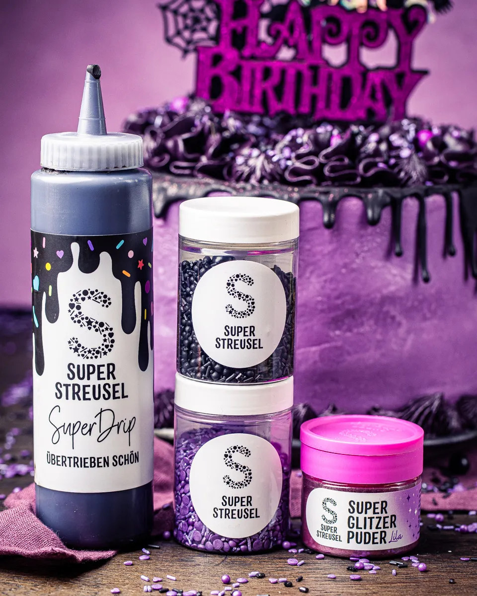 Nahaufnahme eines Wednesday Geburtstagskuchens mit schwarzem Drip, lila Streuseln und Glitzer