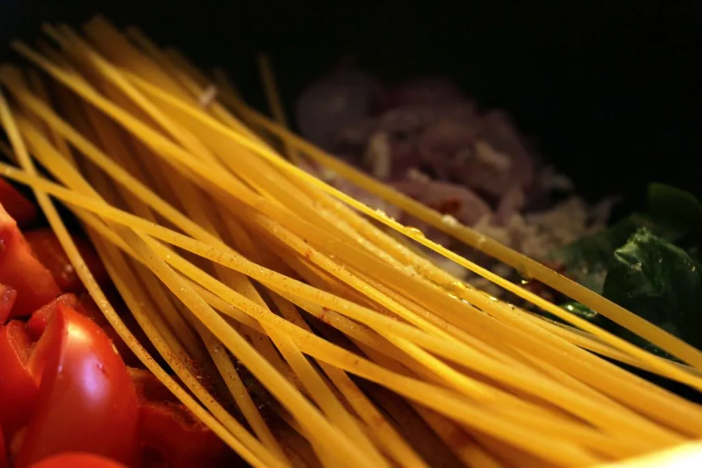Nahaufnahme von Linguine und Gemüse, die in einer Pfanne kochen, während die Nudeln weich werden