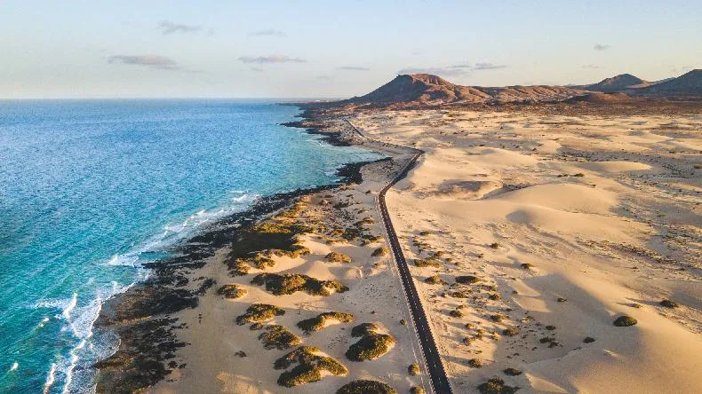 Panoramaaufnahme des breiten, goldenen Sandstrandes von Cofete auf Fuerteventura, umgeben von schroffen Bergen