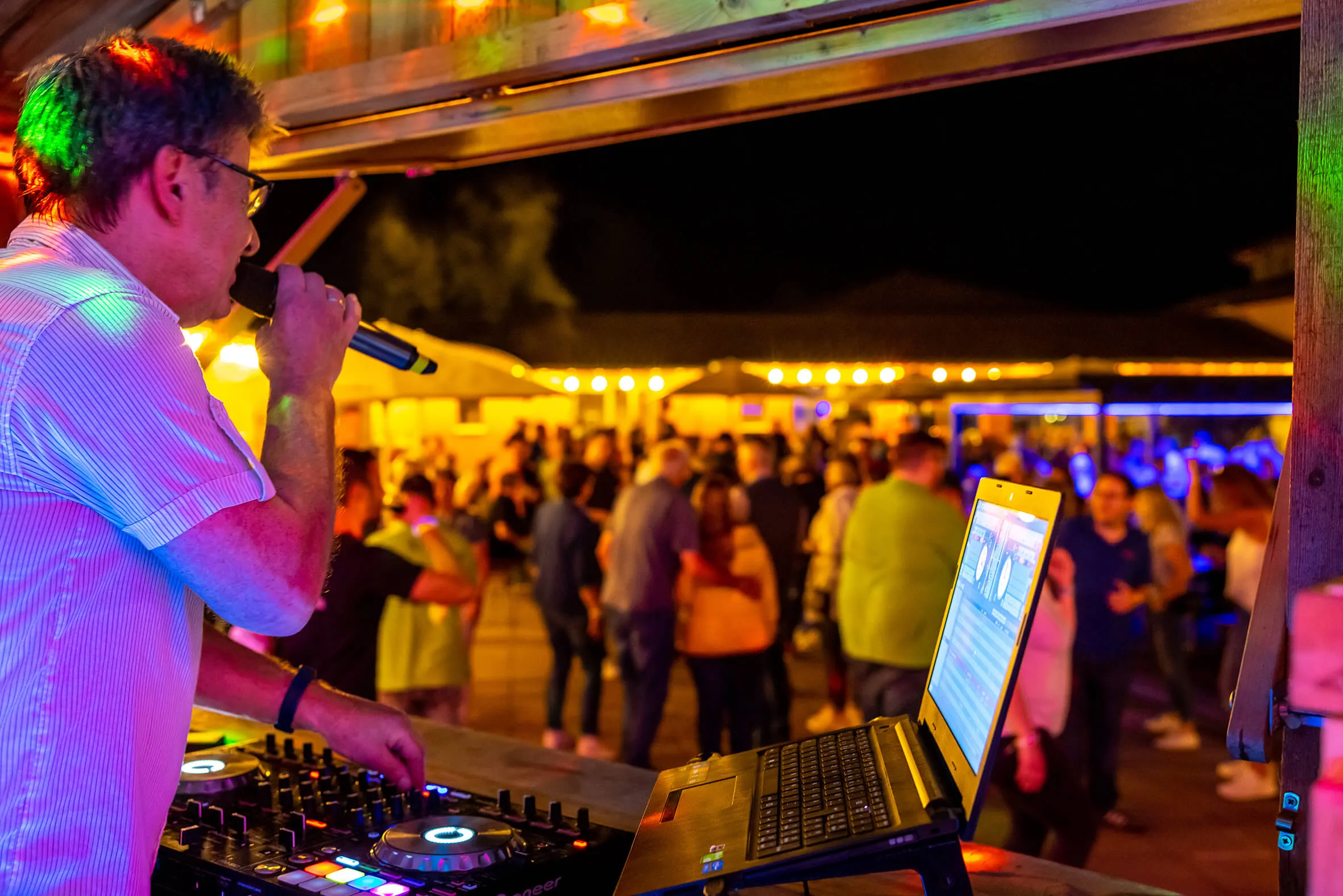 Partygäste tanzen ausgelassen zu den Beats eines DJs in einer hell erleuchteten Diskothek.