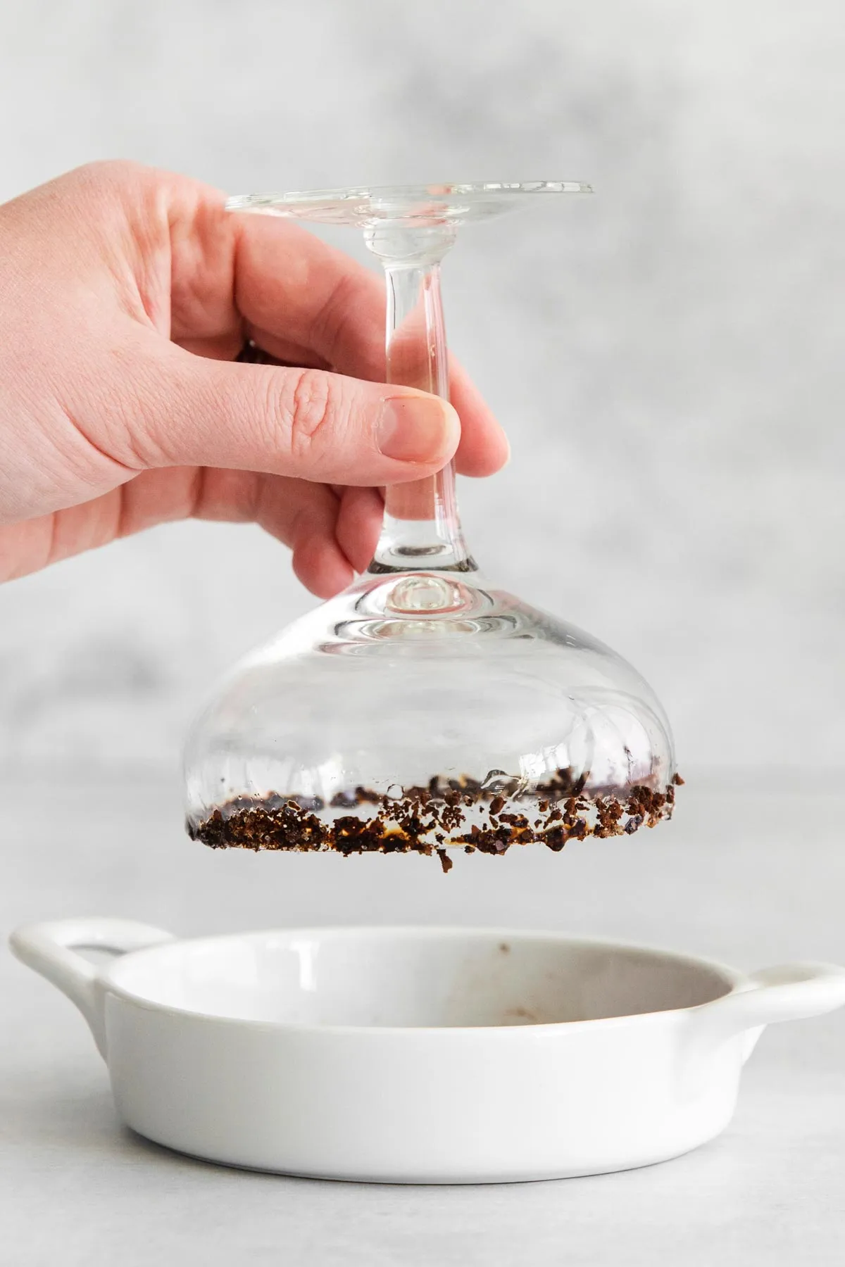 Prozessfoto, das einen Glasbehälter mit Eis und Zutaten für einen veganen Espresso Martini zeigt, wobei eine Hand einen Stiel hält, der in gemahlenem Kaffee getaucht wird