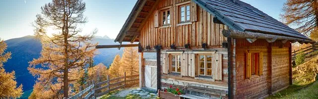 Romantische Almhütte aus Holz, umgeben von herbstlicher Natur und Bergen.