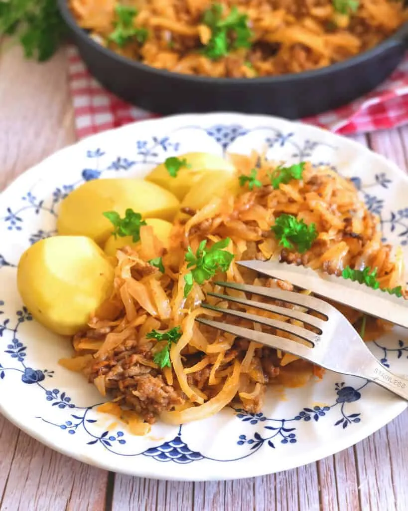 Schmorkohl mit Hackfleisch, serviert mit Pellkartoffeln und einem Klecks Sauerrahm.