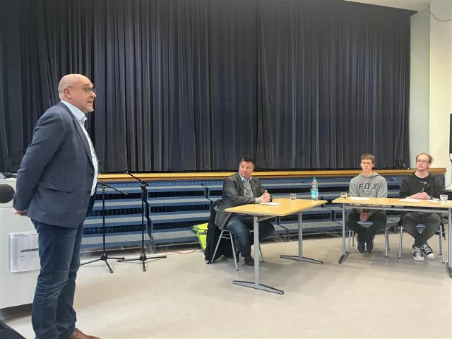 Schulleiter Thorsten Prinz (links) und die Moderatoren Max Weiler und Michel Scherbaum (rechts) begrüßen Boris Mijatovic.