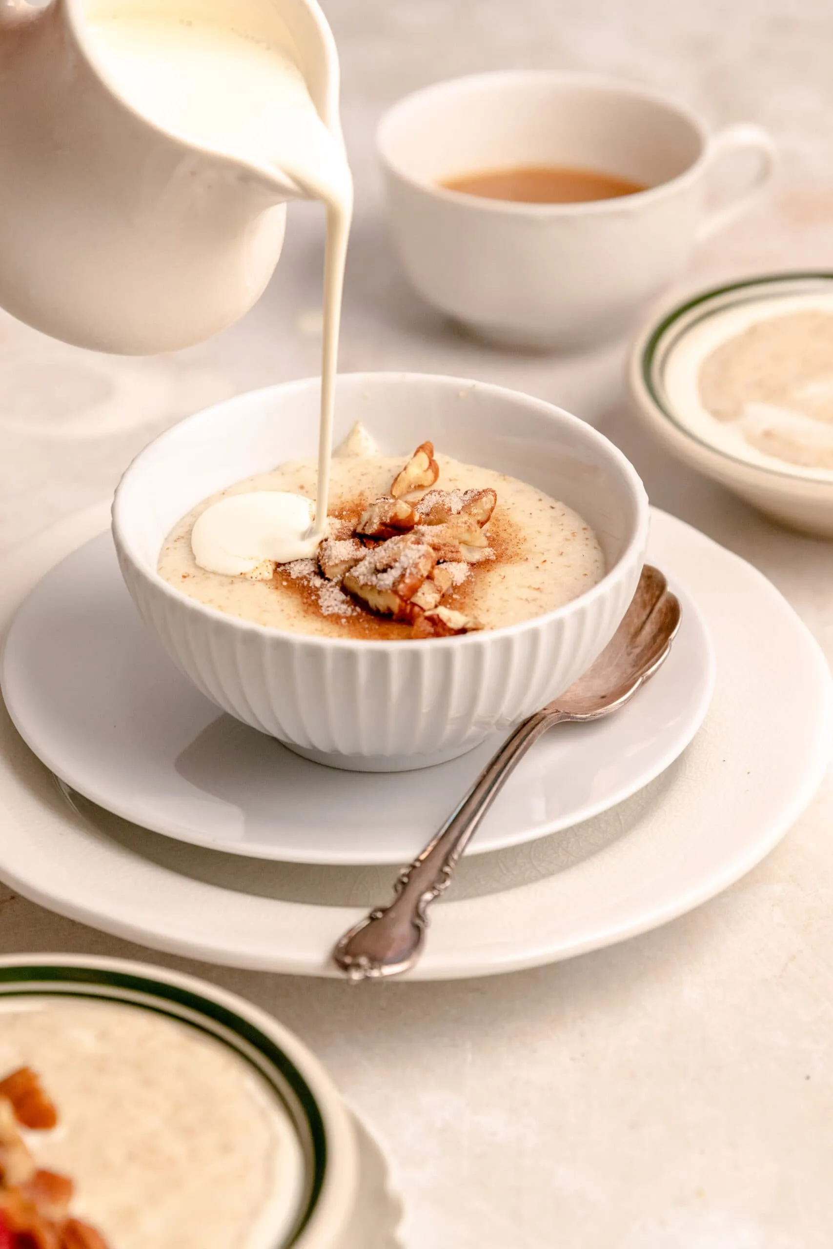 Seitenansicht, wie dicke Sahne über eine Schale Grießbrei mit Pekannüssen und Zimtzucker gegossen wird.