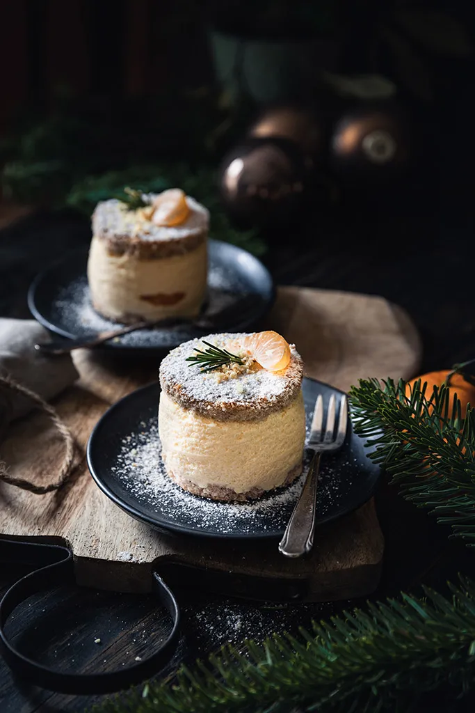 Sieben festliche Mandarinen-Käse-Sahne-Törtchen, fertig gebacken und noch unglasiert, auf einem Backblech angerichtet.