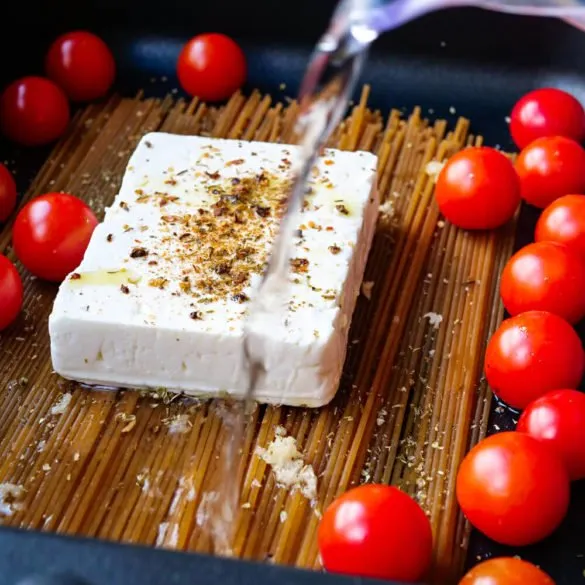 Spaghetti mit Feta und Tomaten in der schwarzen Auflaufform werden mit Wasser begossen.