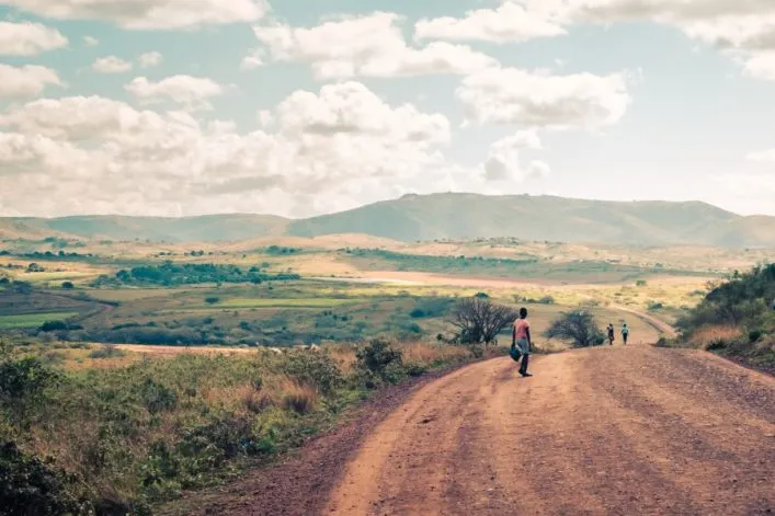 Staubiger Weg durch grüne, hügelige Landschaft in Eswatini mit Wanderern – exotisches Abenteuer