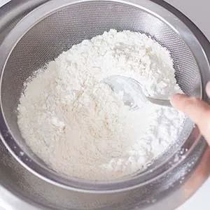 Trockene Zutaten für den Biskuitboden sorgfältig sieben, um eine feine Textur zu gewährleisten