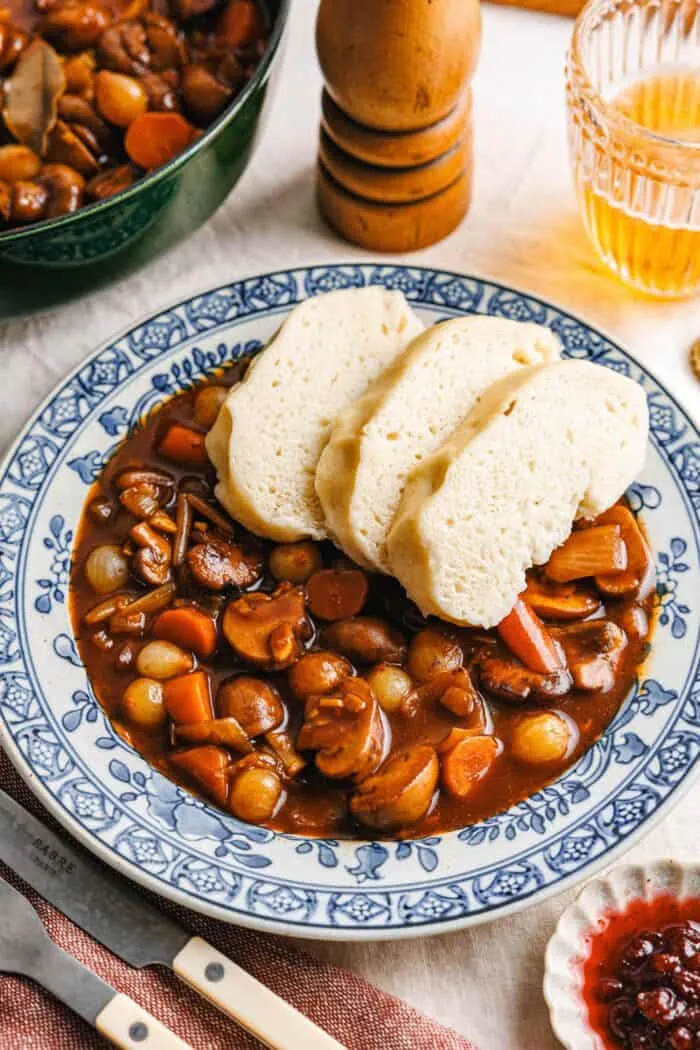Vegane böhmische Knödel, fertig geschnitten, auf einem Teller neben einem Gericht