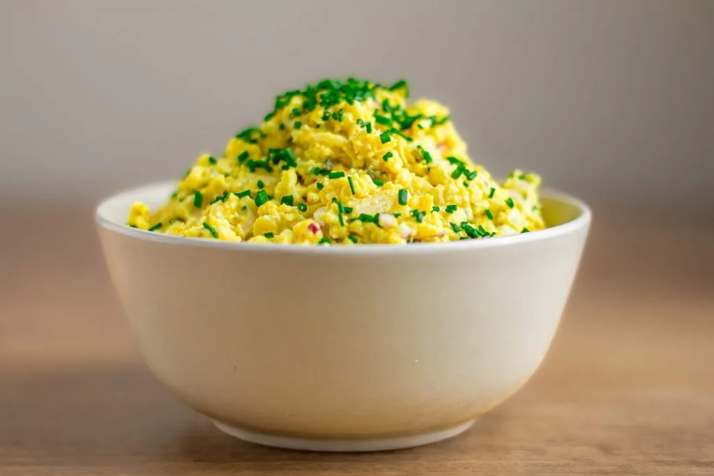 Veganer Eiaufstrich auf einer Scheibe Brot, dekoriert mit frischem Schnittlauch und rosa Pfeffer