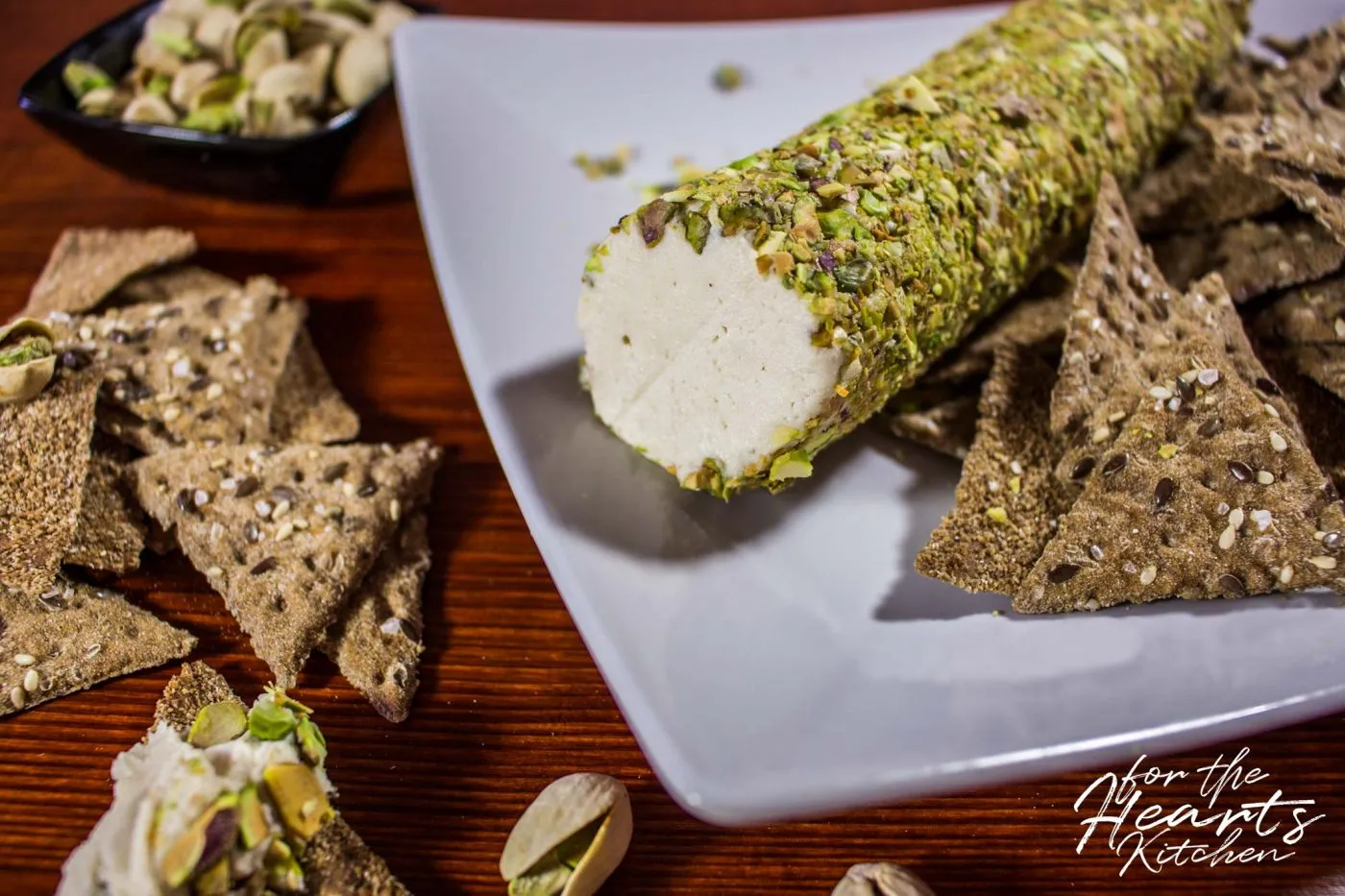 Veganer Ziegenfrischkäse im Pistazienmantel auf einem Holzbrett mit Trauben und Crackern