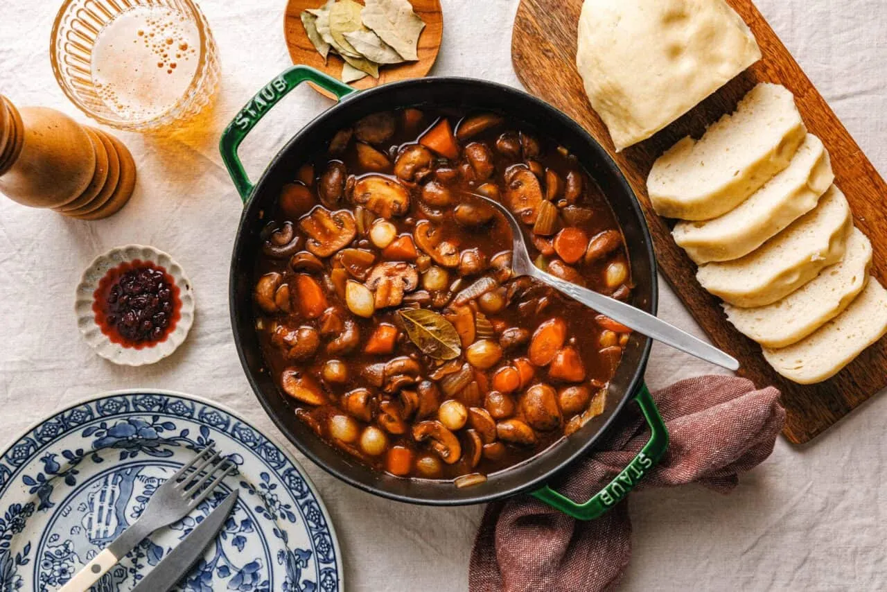 Veganes Biergulasch mit Pilzen und veganen böhmischen Knödeln auf einem Teller, bereit zum Servieren