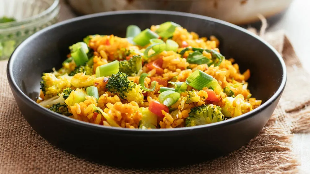 Vegetarische Reispfanne in einer großen Schale, reich an Gemüse und gelb gefärbt vom Kurkuma.