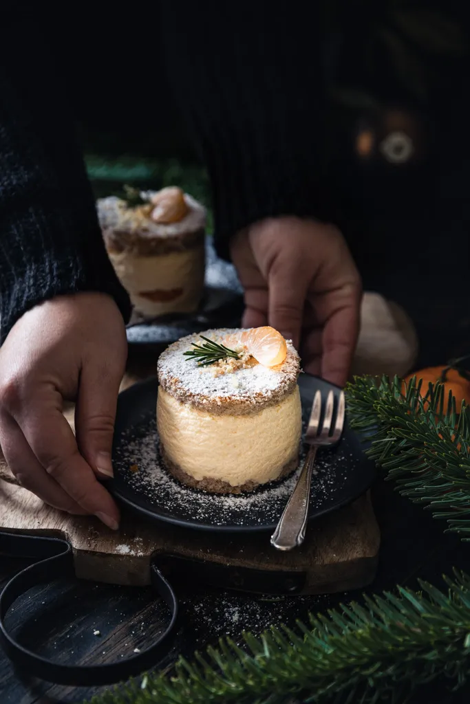 Vier festliche Mandarinen-Käse-Sahne-Törtchen mit Glanz und weihnachtlicher Dekoration, auf einem Holzbrett ansprechend präsentiert.