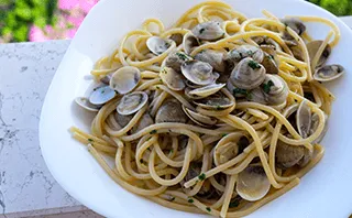 Vincenzo's Vater Paolo lächelt und hält eine Schale frischer Spaghetti Vongole in seinen Händen