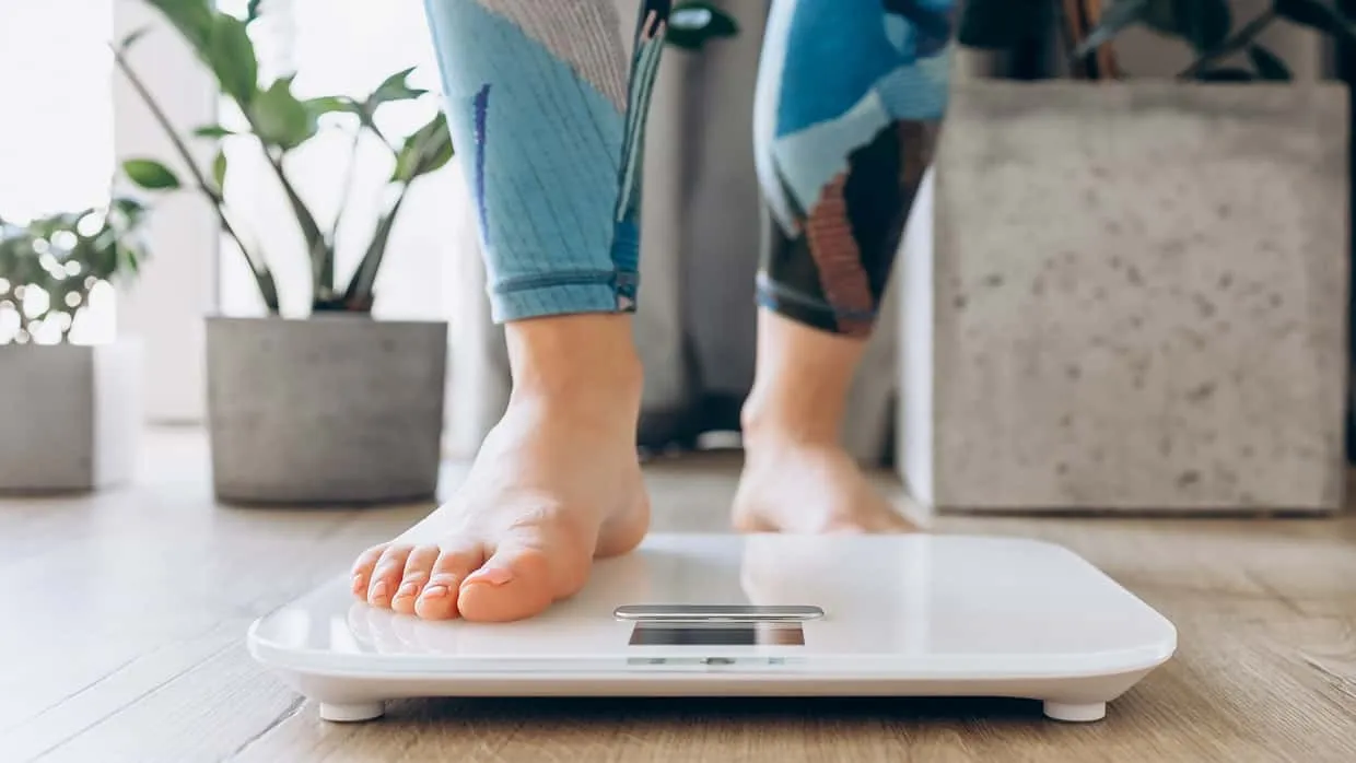 Weibliche Füße auf einer Waage, die den Fortschritt beim Abnehmen dokumentieren und motivieren.