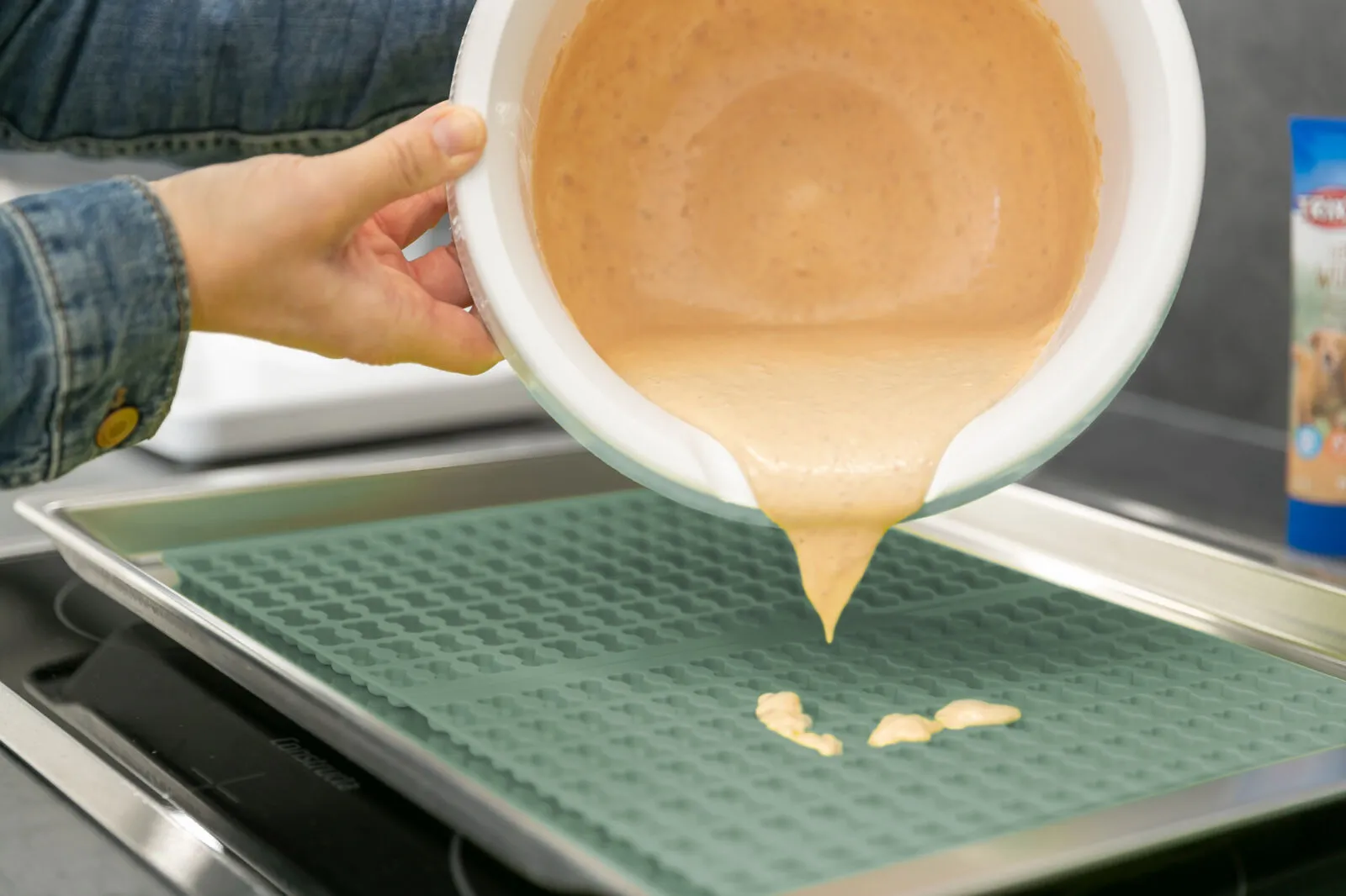 Zahlreiche kleine Hundekekse in Knochenform werden auf einer blauen Backmatte aus dem Ofen genommen