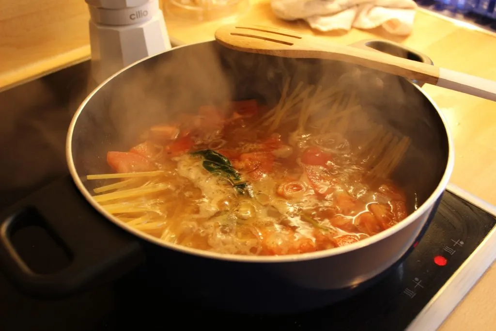 Zubereitete One Pan Pasta in einer Pfanne, garniert mit frischem Basilikum und Parmesan