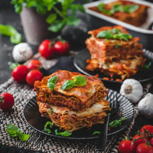 Zwei appetitliche Stücke veganer Lasagne auf schwarzen Tellern, garniert mit frischem Basilikum