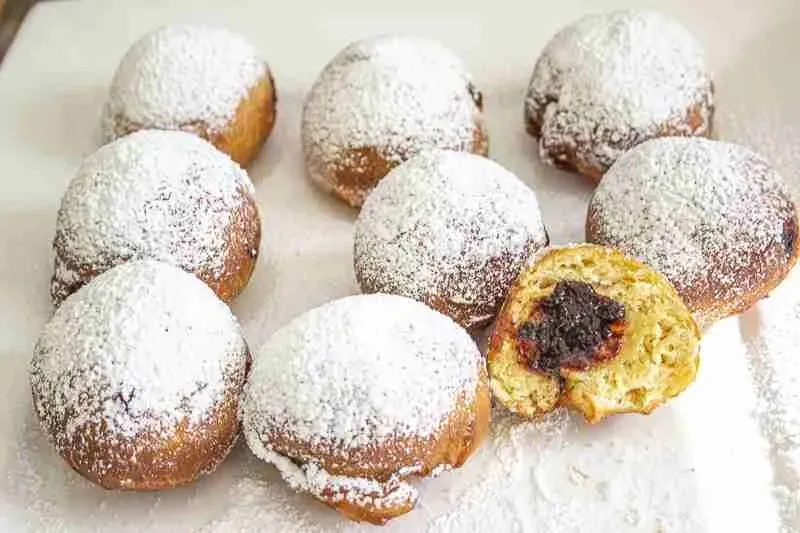 Zwei Berliner Pfannkuchen, einer mit Puderzucker bestreut, einer mit Marmeladenfüllung sichtbar