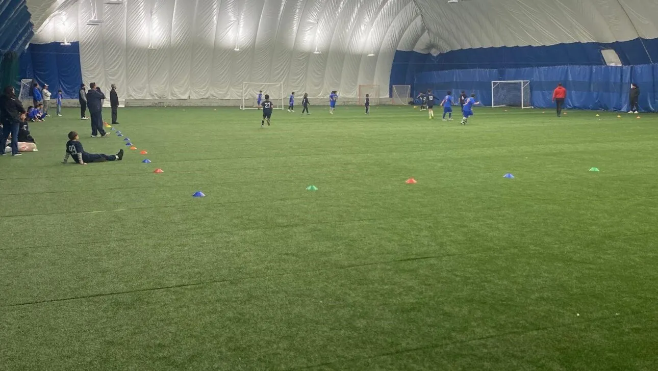 Innen-Sportanlage mit Kunstrasen, Spieler trainieren auf dem Feld und bunte Kegel sind auf dem Boden angeordnet.