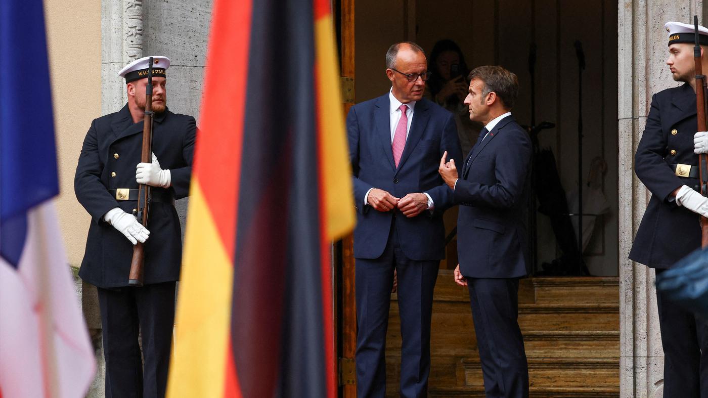 Angela Merkel und Brigitte Macron teilen eine herzliche Umarmung bei einem Staatsbesuch, symbolisch für die deutsch-französische Freundschaft.