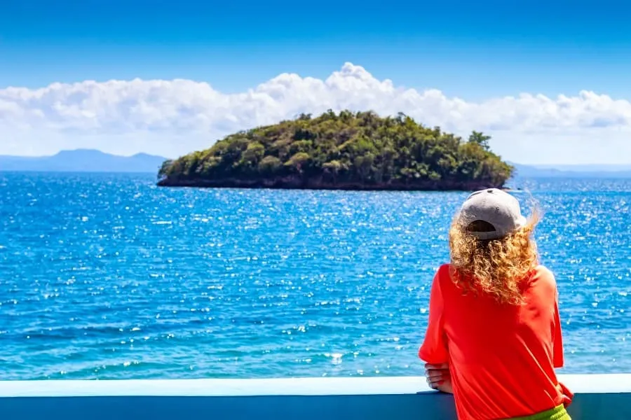 Ein Urlauber im roten Shirt blickt aufs Meer der Dominikanischen Republik, kleine Insel und blauer Himmel im Hintergrund.