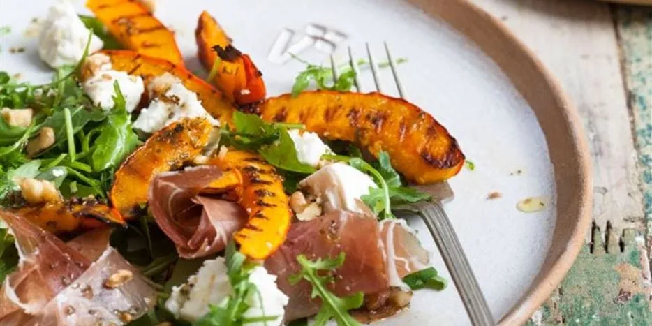 Fertig angerichteter Teller mit gegrillten Kürbisspalten, Rucola und Nüssen