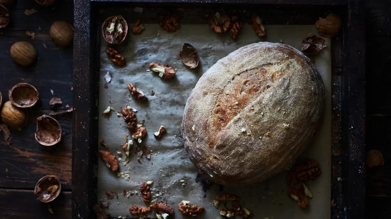 Frontalsicht: Ein Walnussbrot auf einen backblech. Drumherum liegen offene und geschlossene Walnussschalen.