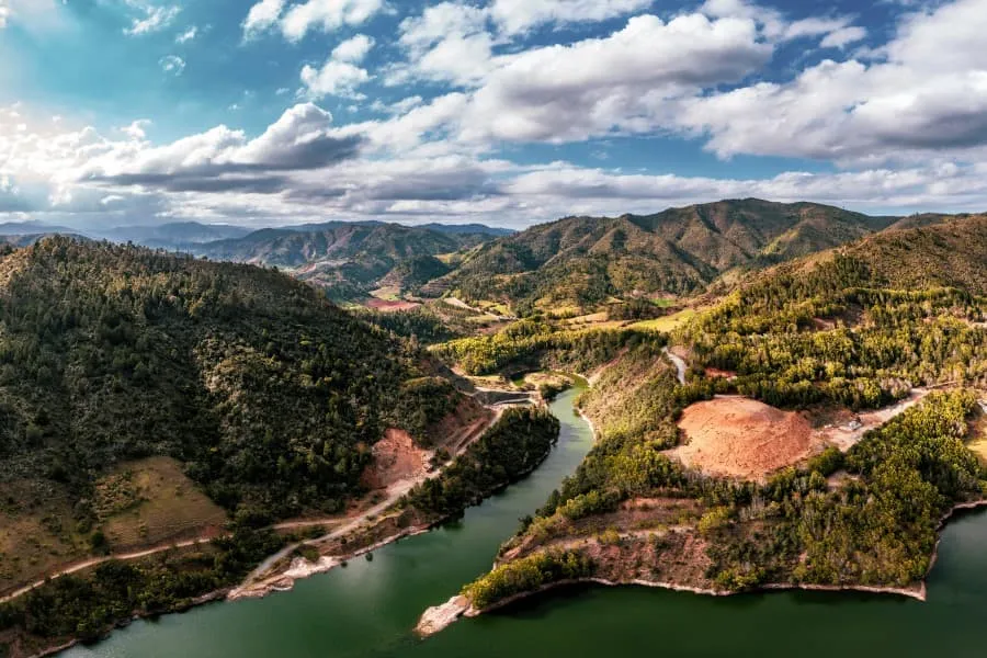 Grüne Hügellandschaft mit einem gewundenen Fluss im Herzen der Dominikanischen Republik, ideal für einen Natur-Urlaub. Wolken schmücken den blauen Himmel.