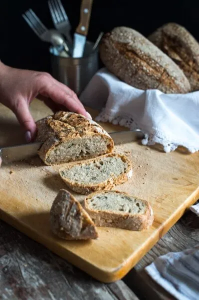 Jemand schneidet ein helles Brot auf einem Holzbrett in Scheiben