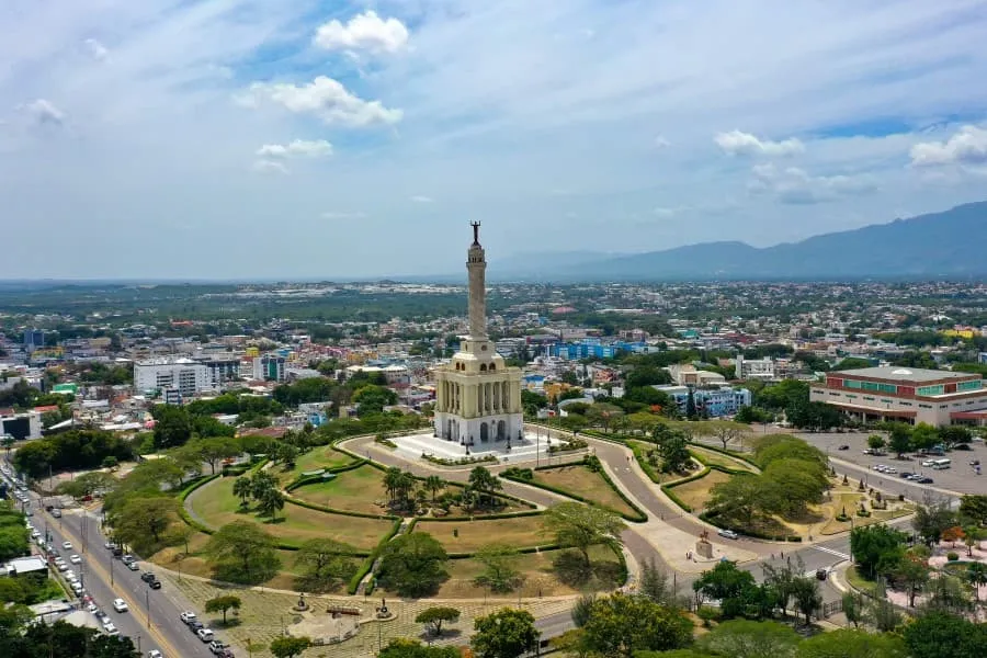 Luftaufnahme des Monumento de Santiago in der Dominikanischen Republik, umgeben von grünen Parks und belebten Straßen, mit bergen im Hintergrund.