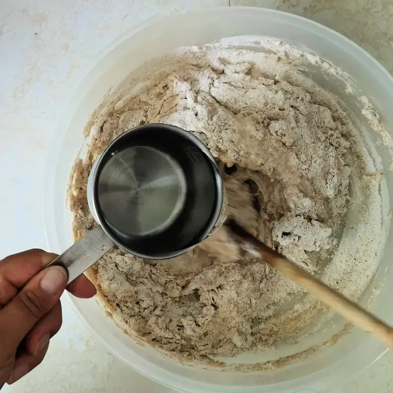 Mehl und Wasser zum Sauerteig hinzufügen