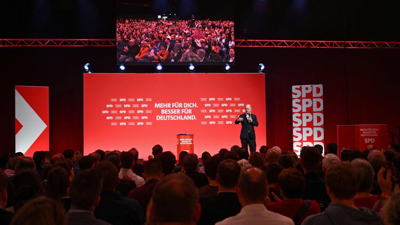 Olaf Scholz spricht auf einer Wahlkampfveranstaltung, im Hintergrund Fahnen der SPD und Deutschland