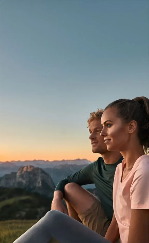Paar sitzt auf Berggipfel und genießt den Sonnenuntergang über den Alpen.
