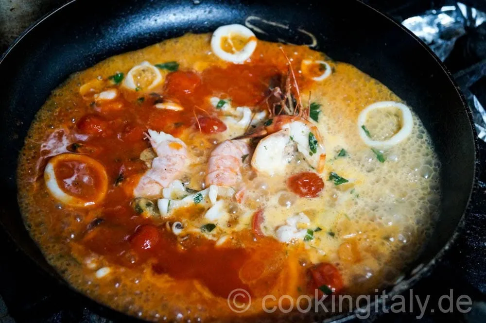 Passierte Tomaten und Gewürze köcheln in der Pfanne mit den Meeresfrüchten.