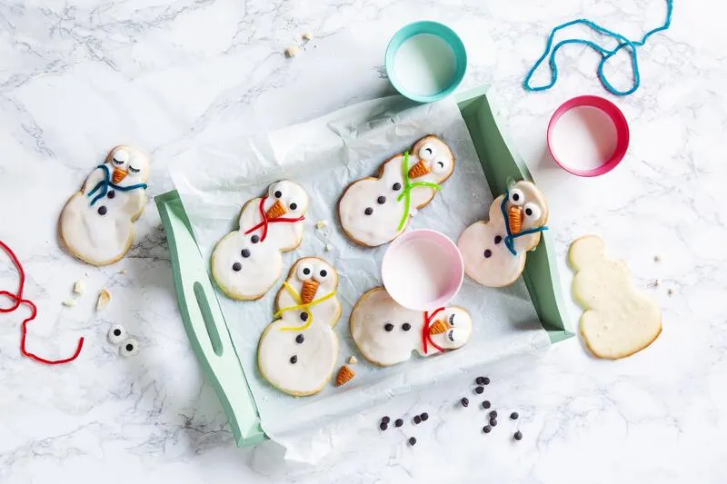Schneemänner-Plätzchen mit Zuckerguss und Dekoration auf grünem Tablett
